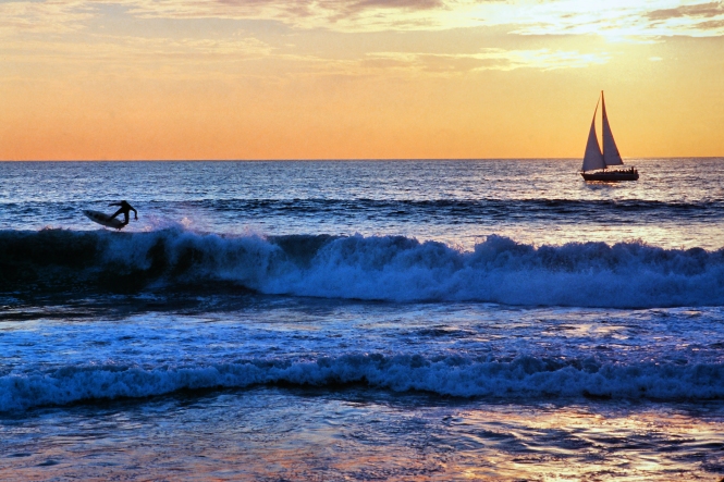 Sailboat and surfer off the Manhattan Beach, California coast at sunset.